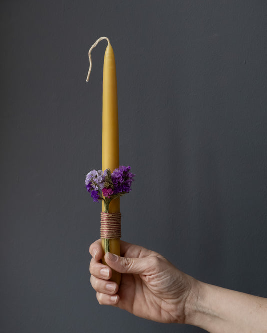 Hand holding a beeswax Easter candle decorated with dried flowers