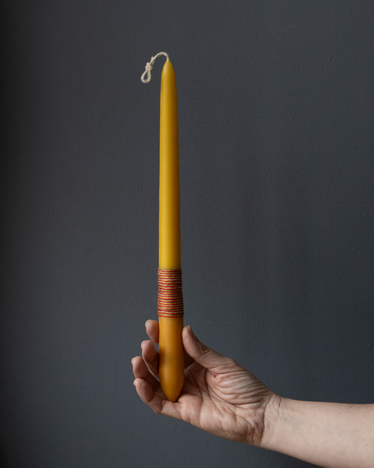 Hand holding a beeswax candle with naturally dyed base and wrapped thread.