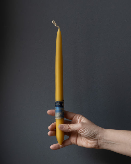 Hand holding a beeswax candle with wrapped thread detail.
