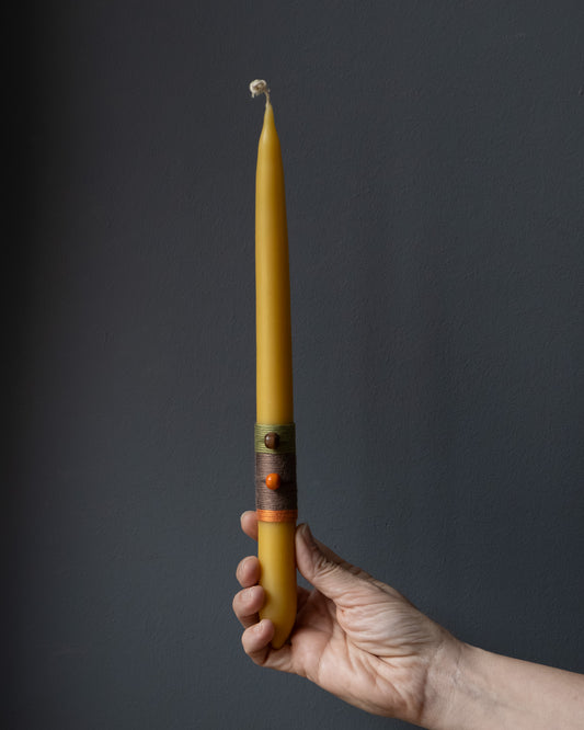 Hand holding a beeswax candle with wrapped thread detail.