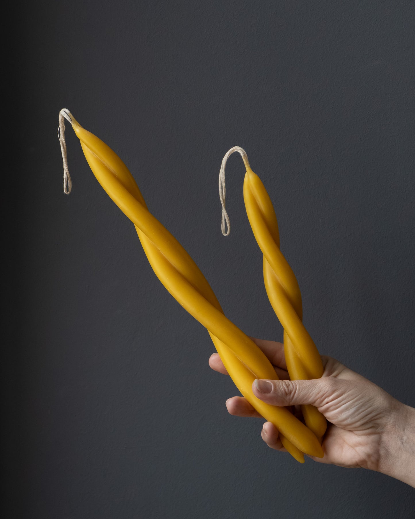 Hand holding two twisted beeswax candles in different sizes