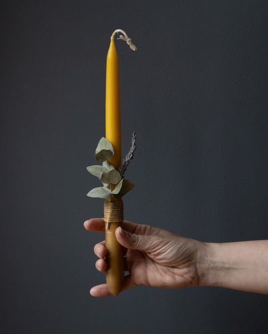 Hand holding a beeswax candle with eucalyptus and lavender