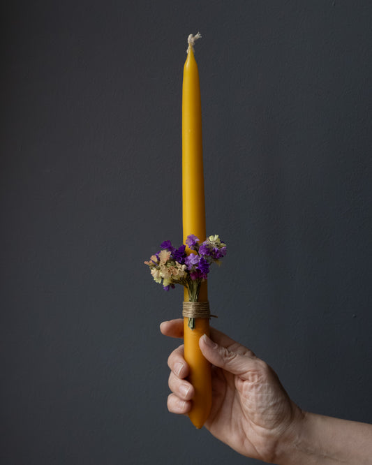 Hand holding a beeswax candle decorated with dried flowers.