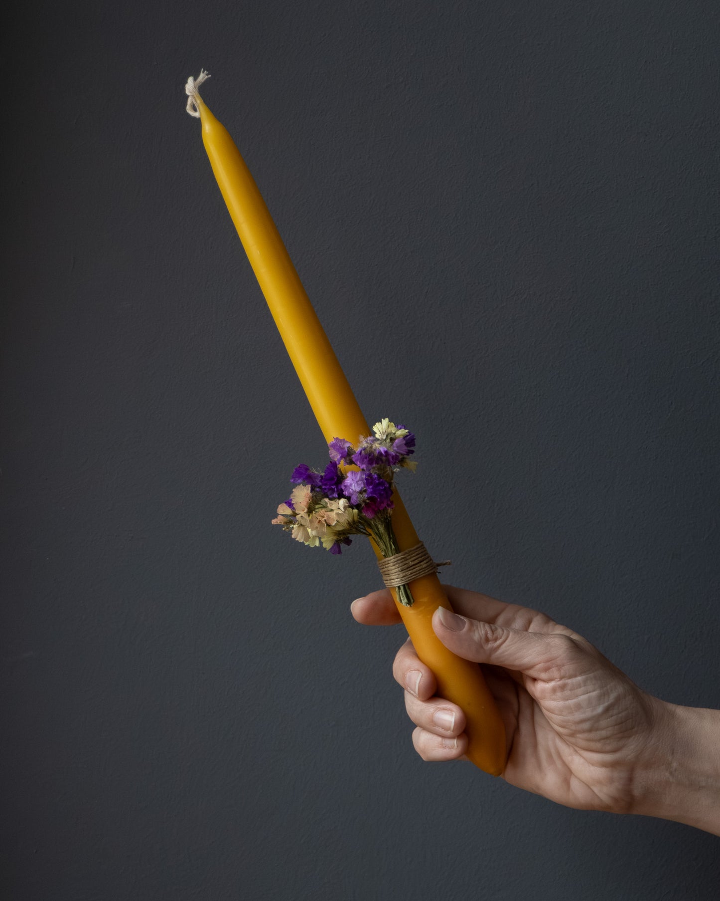 Hand holding a beeswax candle decorated with dried flowers.