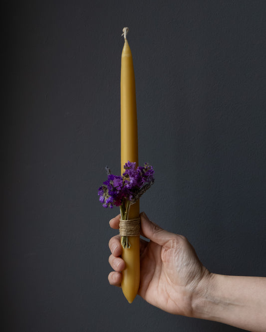 Hand holding a beeswax Easter candle decorated with dried flowers