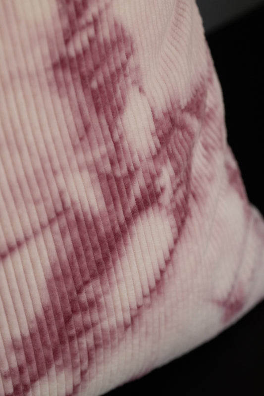 Detail of organic cotton corduroy fabric dyed with cochineal in fuchsia pink, showing detailed tie-dye texture.