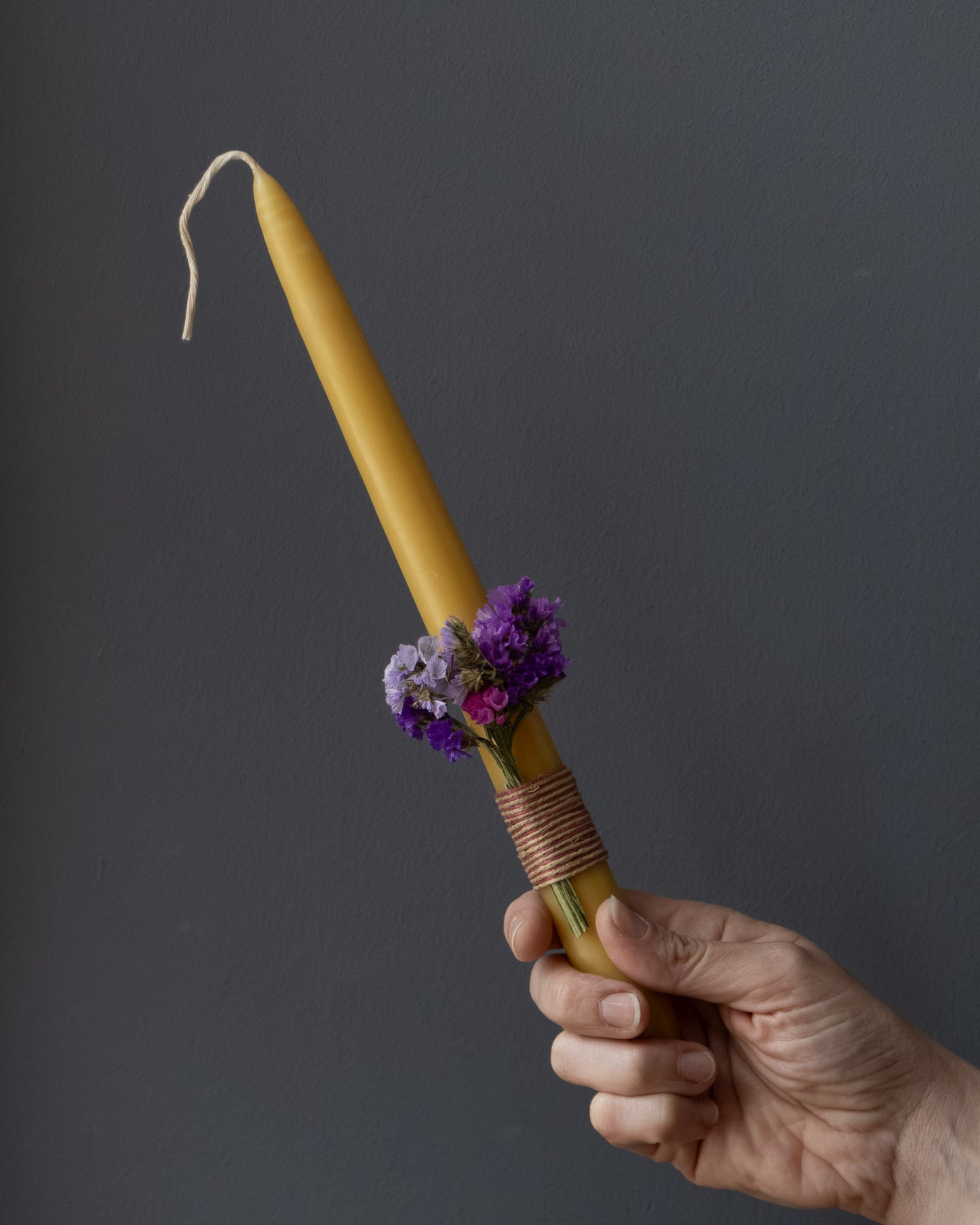 Hand holding a beeswax Easter candle decorated with dried flowers