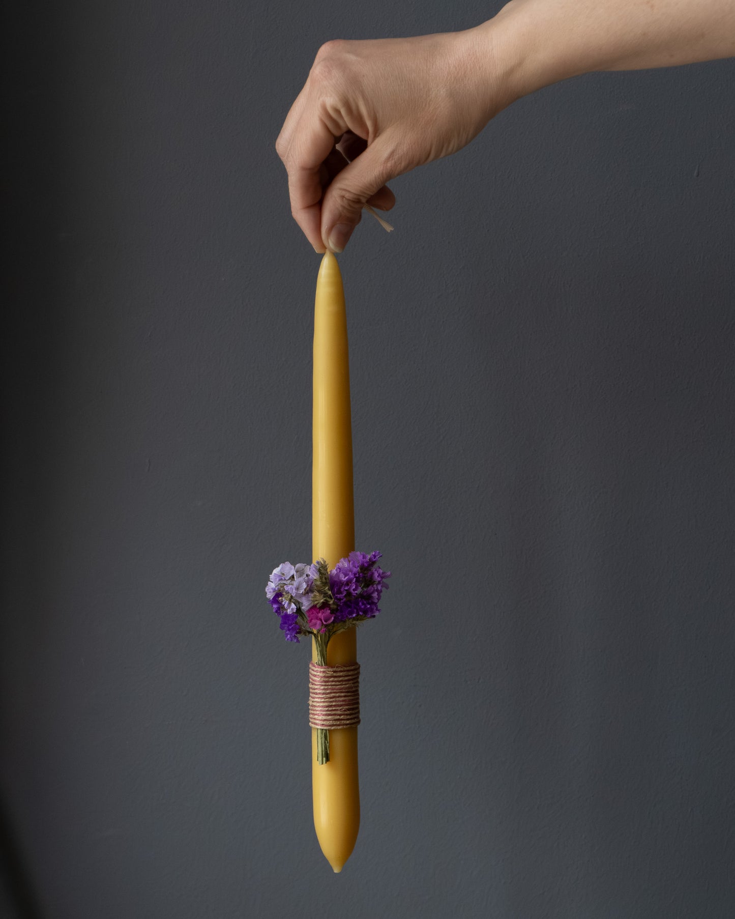 Hand holding a beeswax Easter candle decorated with dried flowers