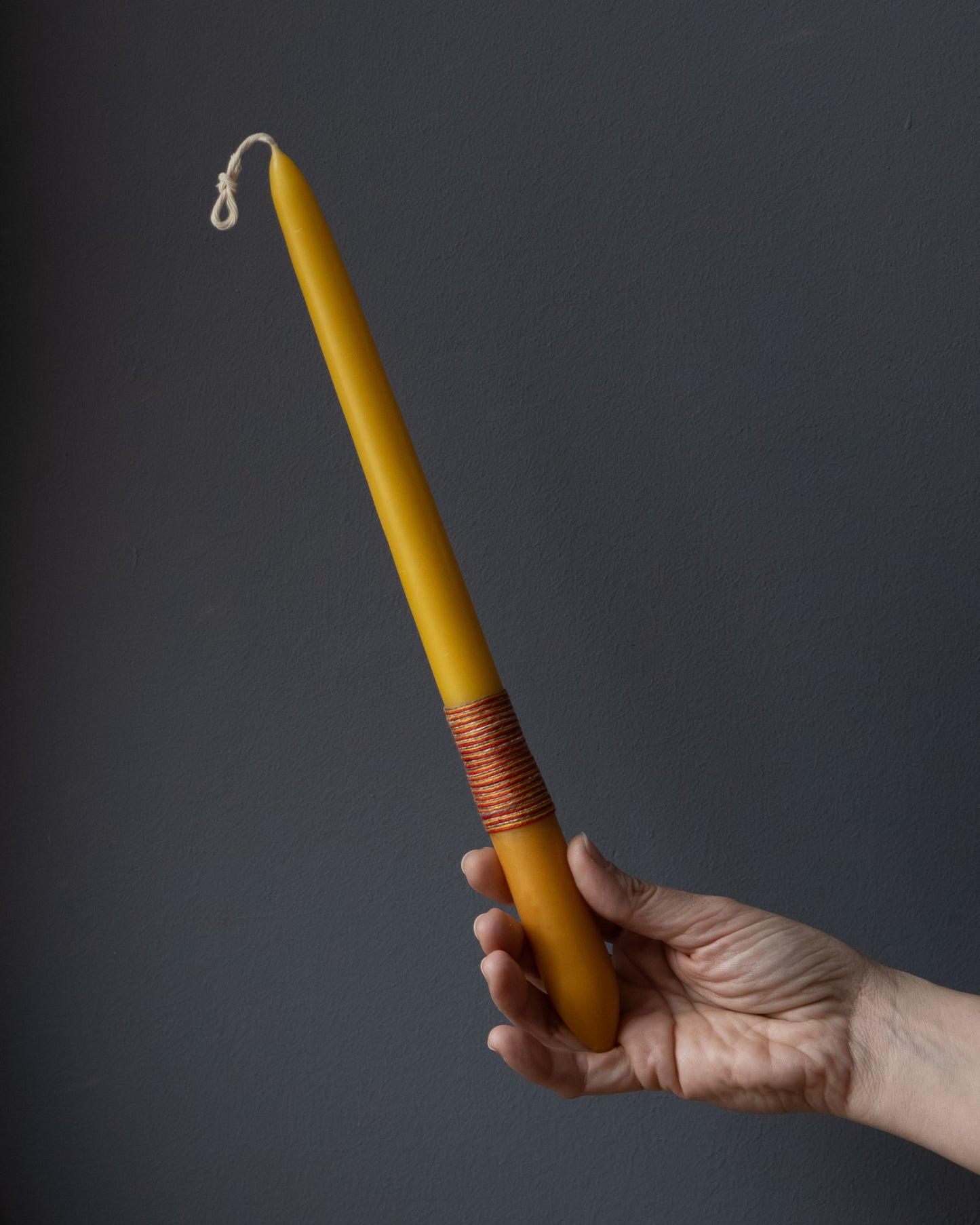 Hand holding a beeswax candle with naturally dyed base and wrapped thread.
