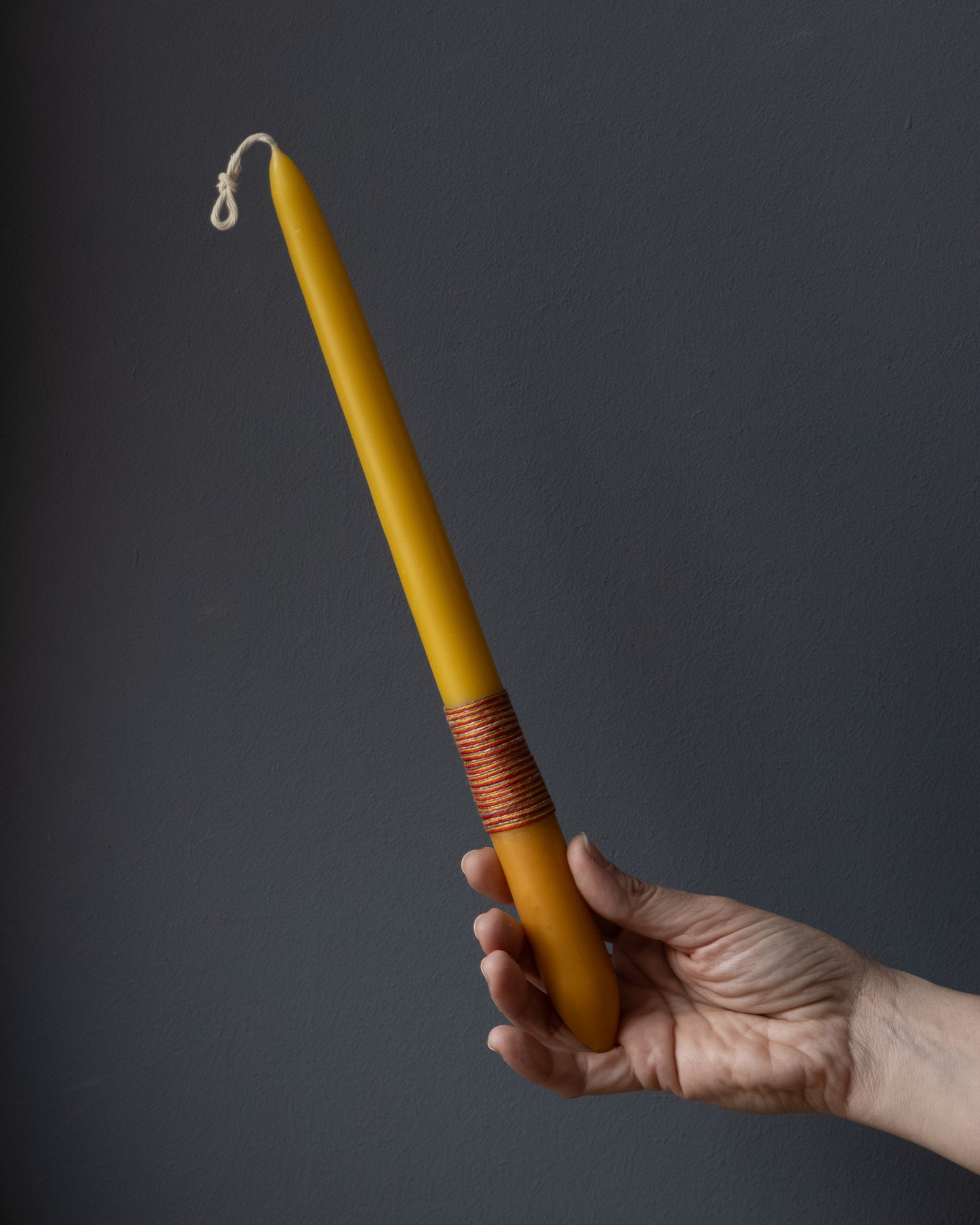 Hand holding a beeswax candle with naturally dyed base and wrapped thread.