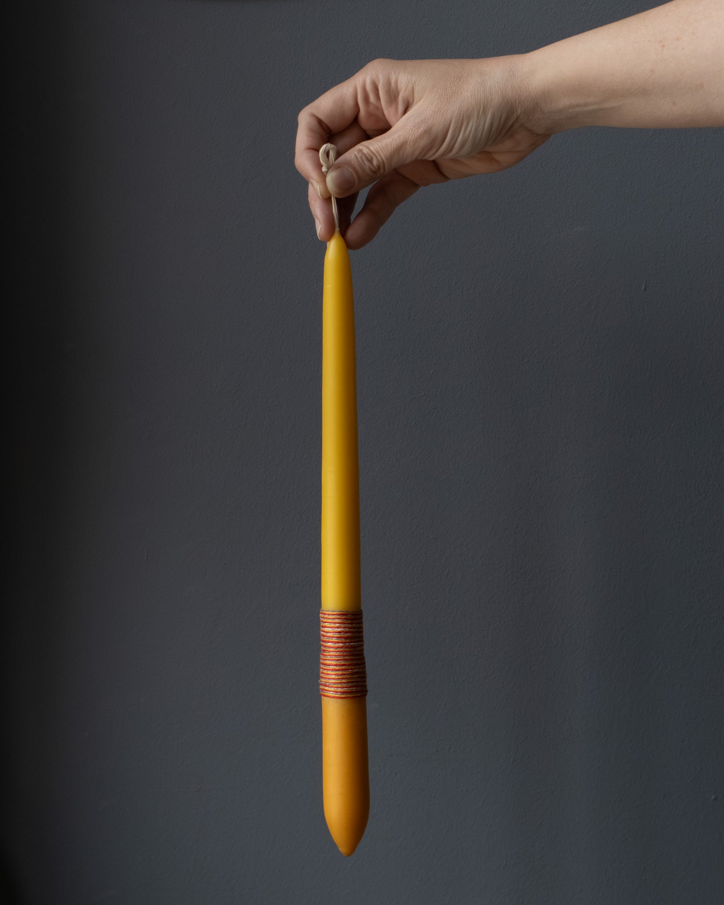 Hand holding a beeswax candle with naturally dyed base and wrapped thread.