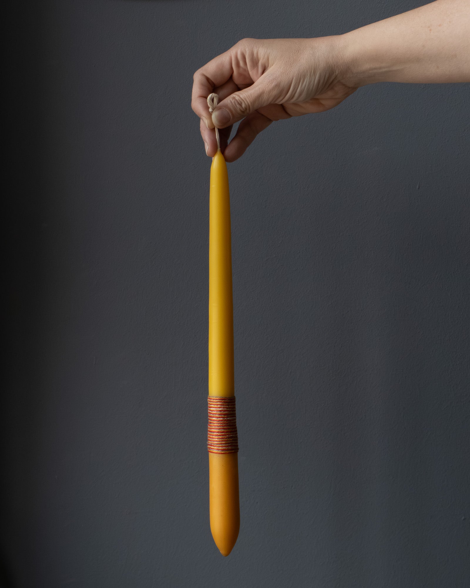 Hand holding a beeswax candle with naturally dyed base and wrapped thread.
