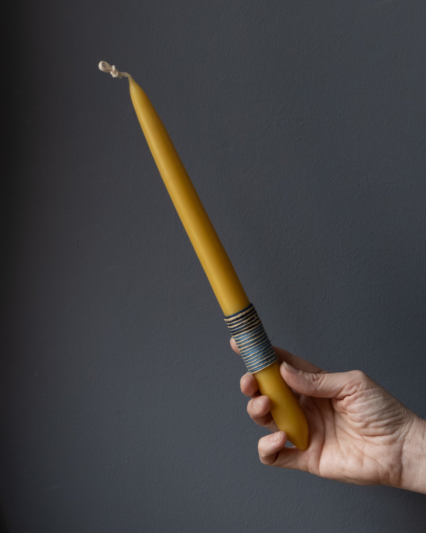 Hand holding a beeswax candle with wrapped thread detail.