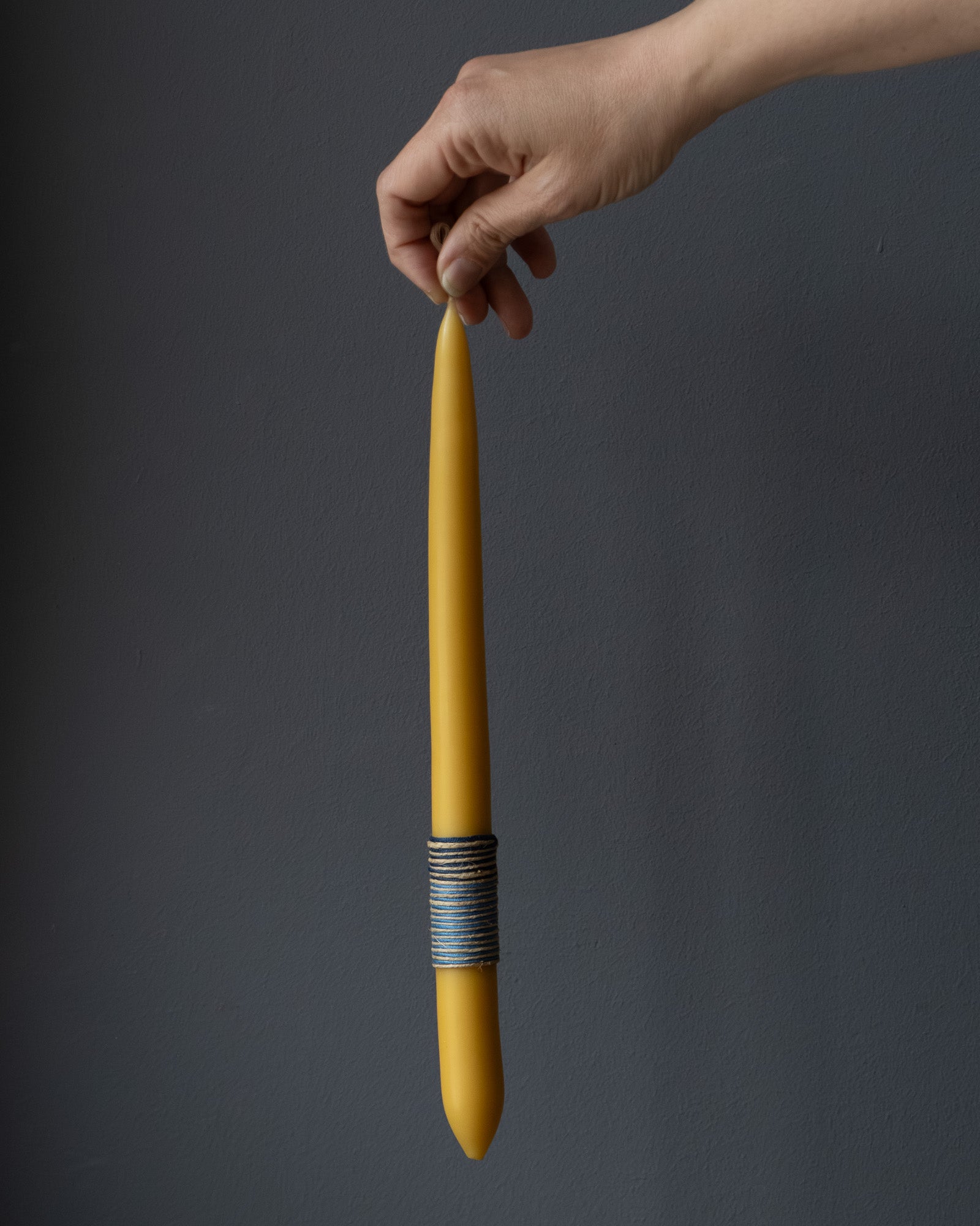 Hand holding a beeswax candle with wrapped thread detail.