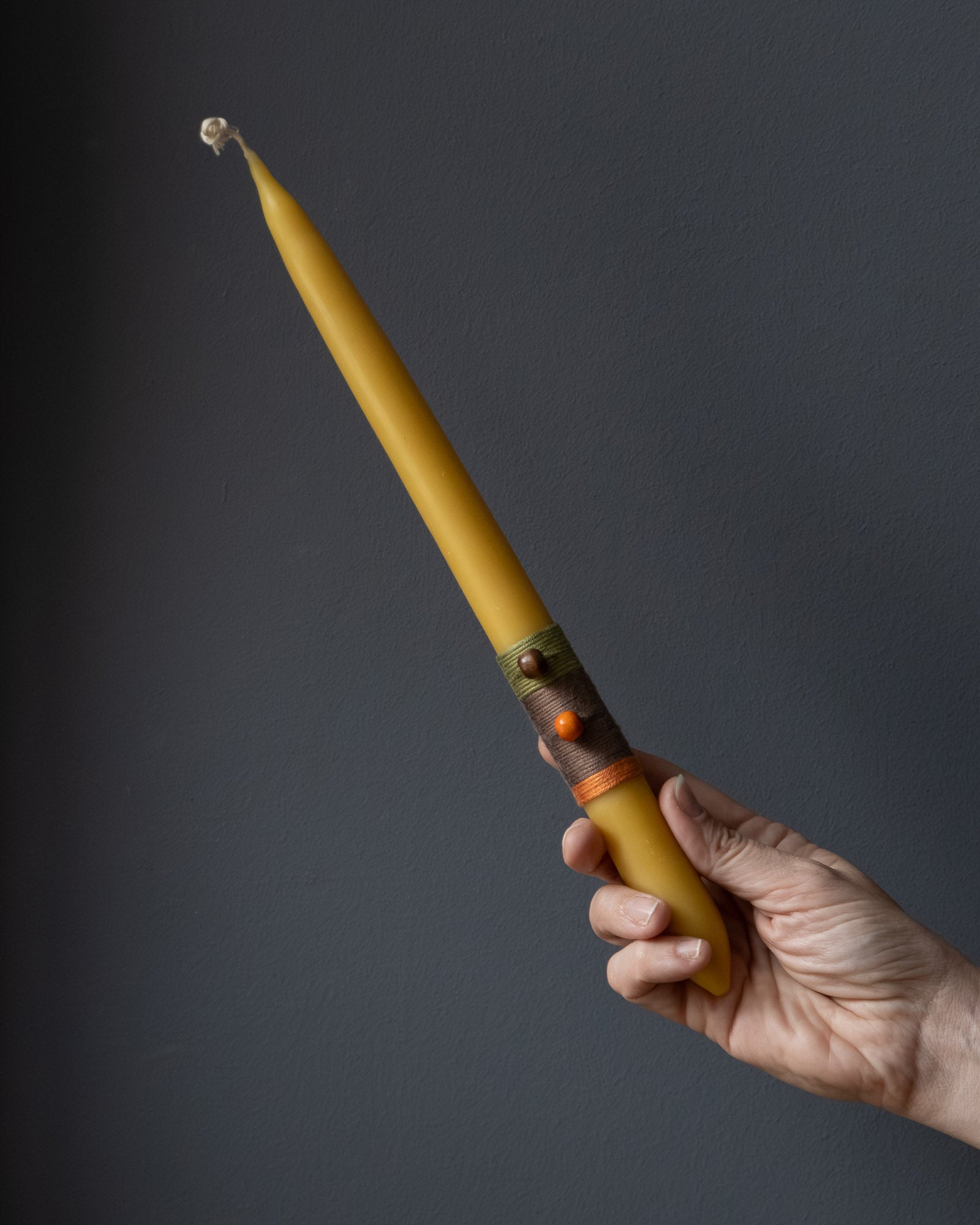 Hand holding a beeswax candle with wrapped thread detail.