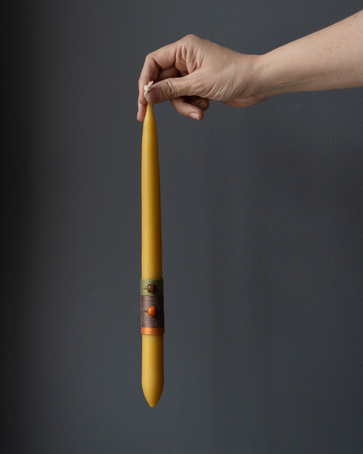 Hand holding a beeswax candle with wrapped thread detail.