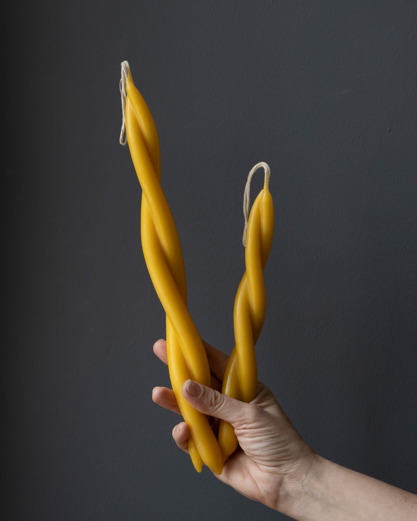 Hand holding two twisted beeswax candles in different sizes