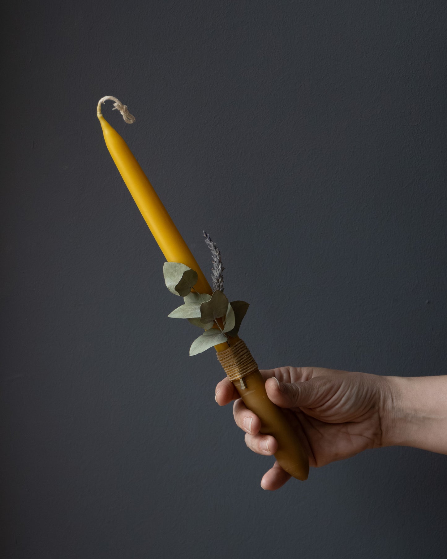 Hand holding a beeswax candle with eucalyptus and lavender