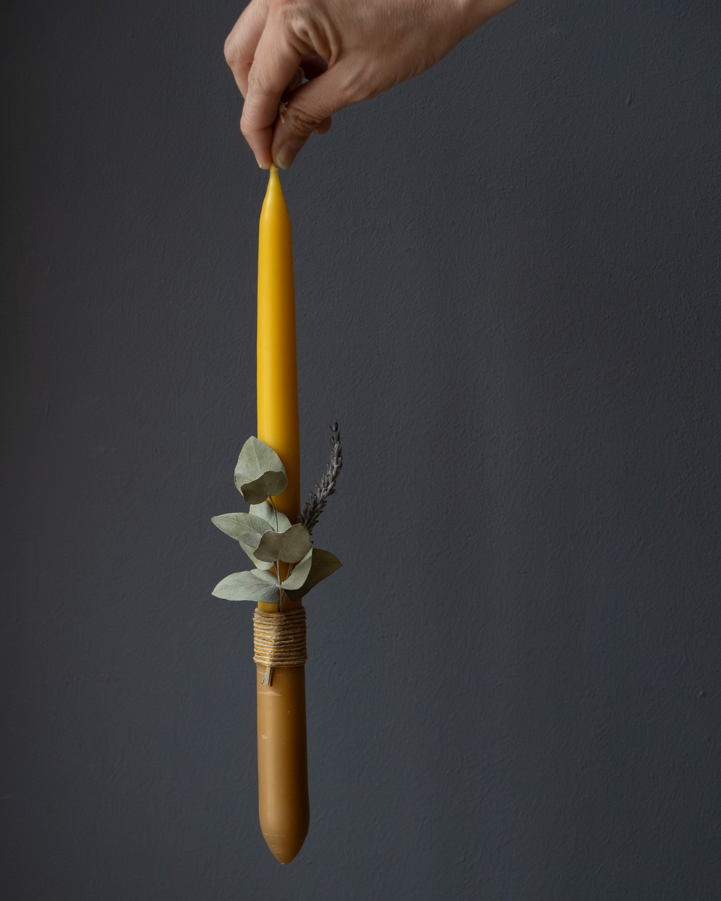 Hand holding a beeswax candle with eucalyptus and lavender