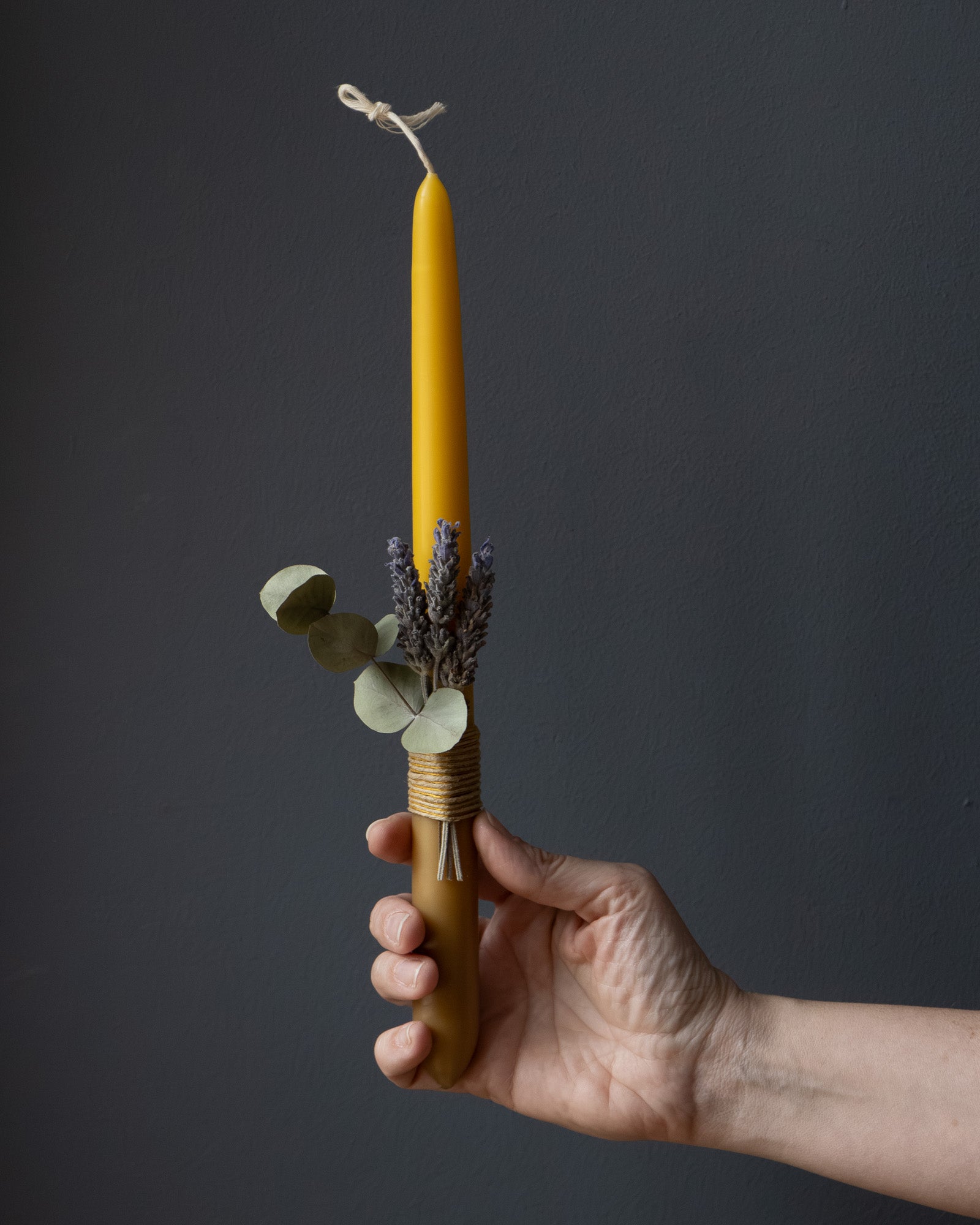 Hand holding a beeswax candle with eucalyptus and lavender