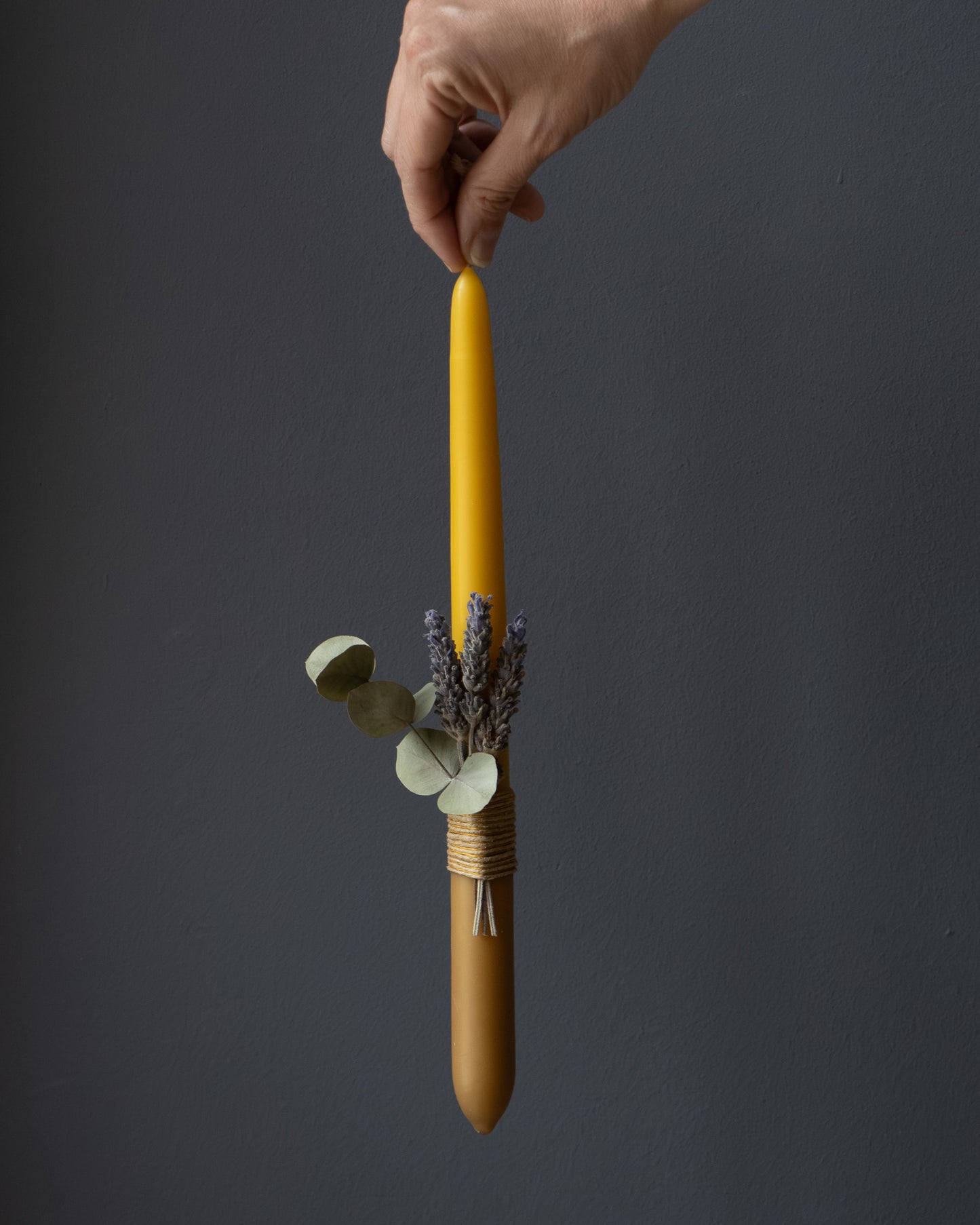Hand holding a beeswax candle with eucalyptus and lavender