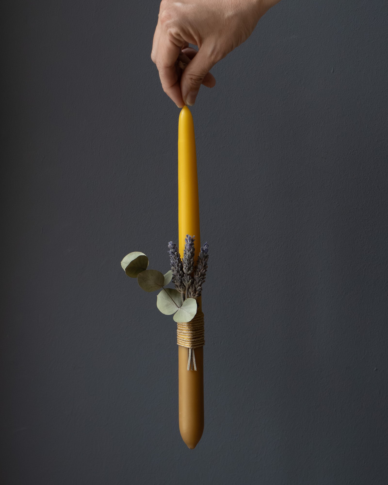 Hand holding a beeswax candle with eucalyptus and lavender