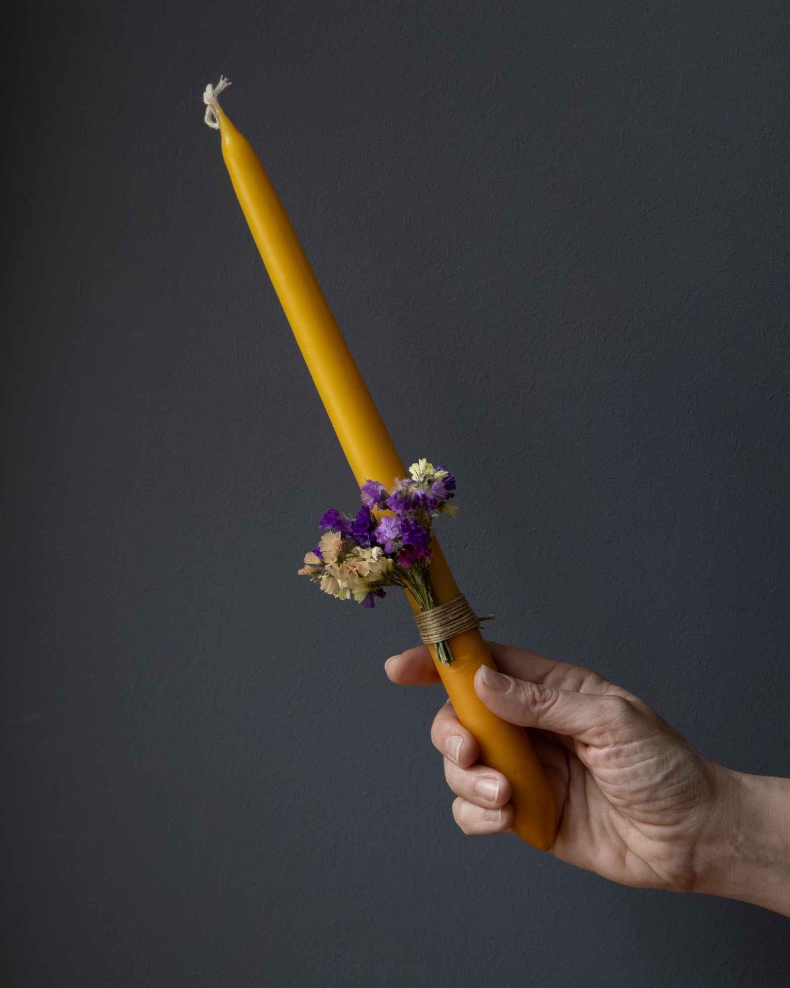 Hand holding a beeswax candle decorated with dried flowers.