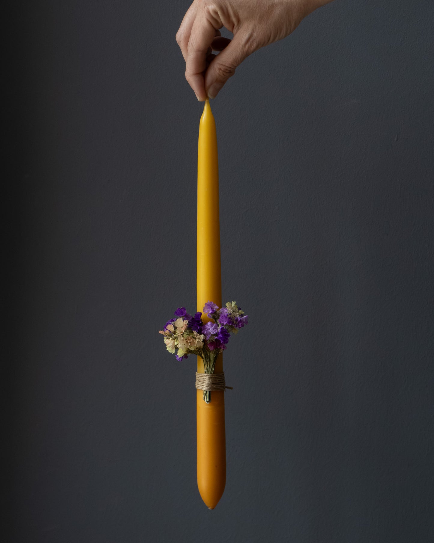 Hand holding a beeswax candle decorated with dried flowers.