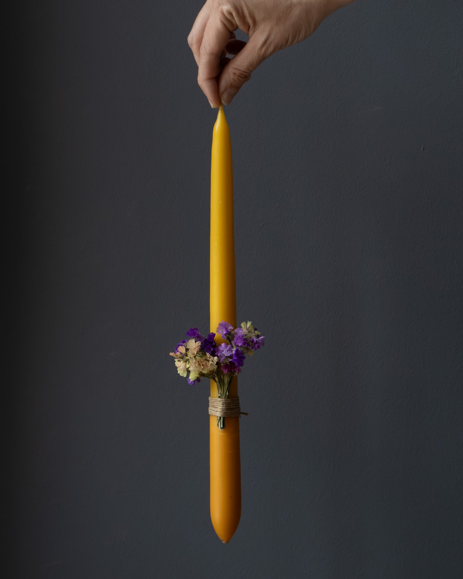 Hand holding a beeswax candle decorated with dried flowers.