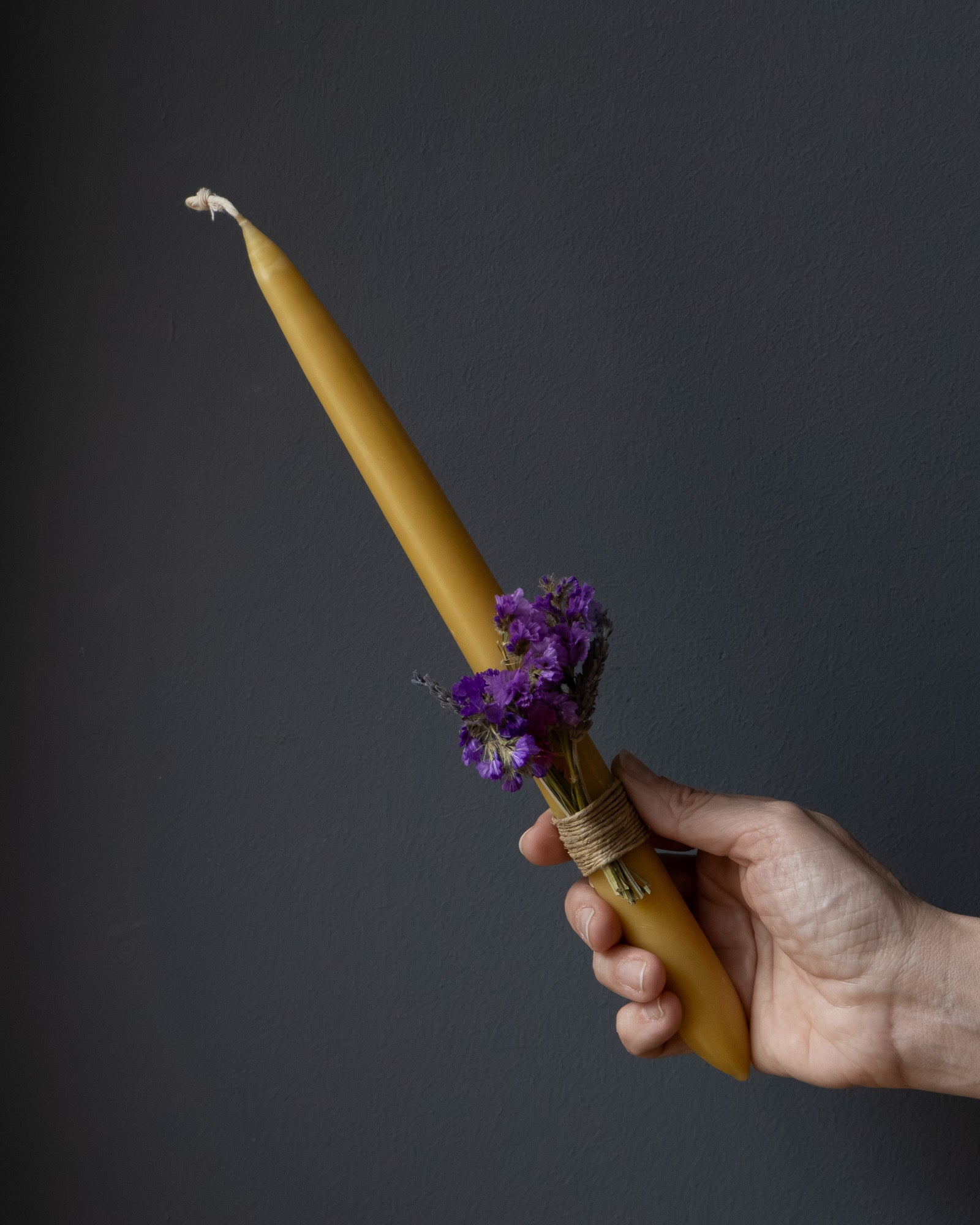 Hand holding a beeswax Easter candle decorated with dried flowers