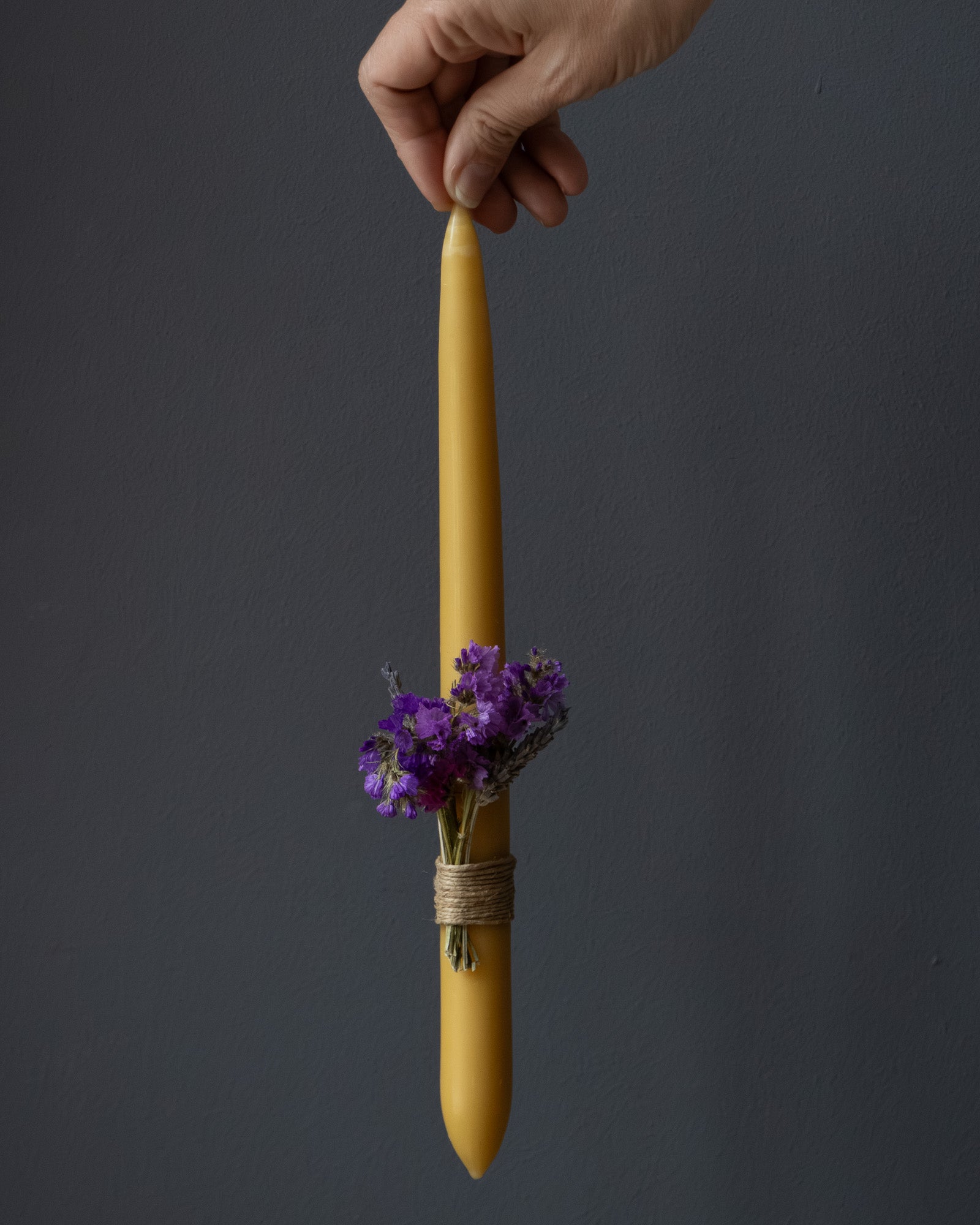 Hand holding a beeswax Easter candle decorated with dried flowers
