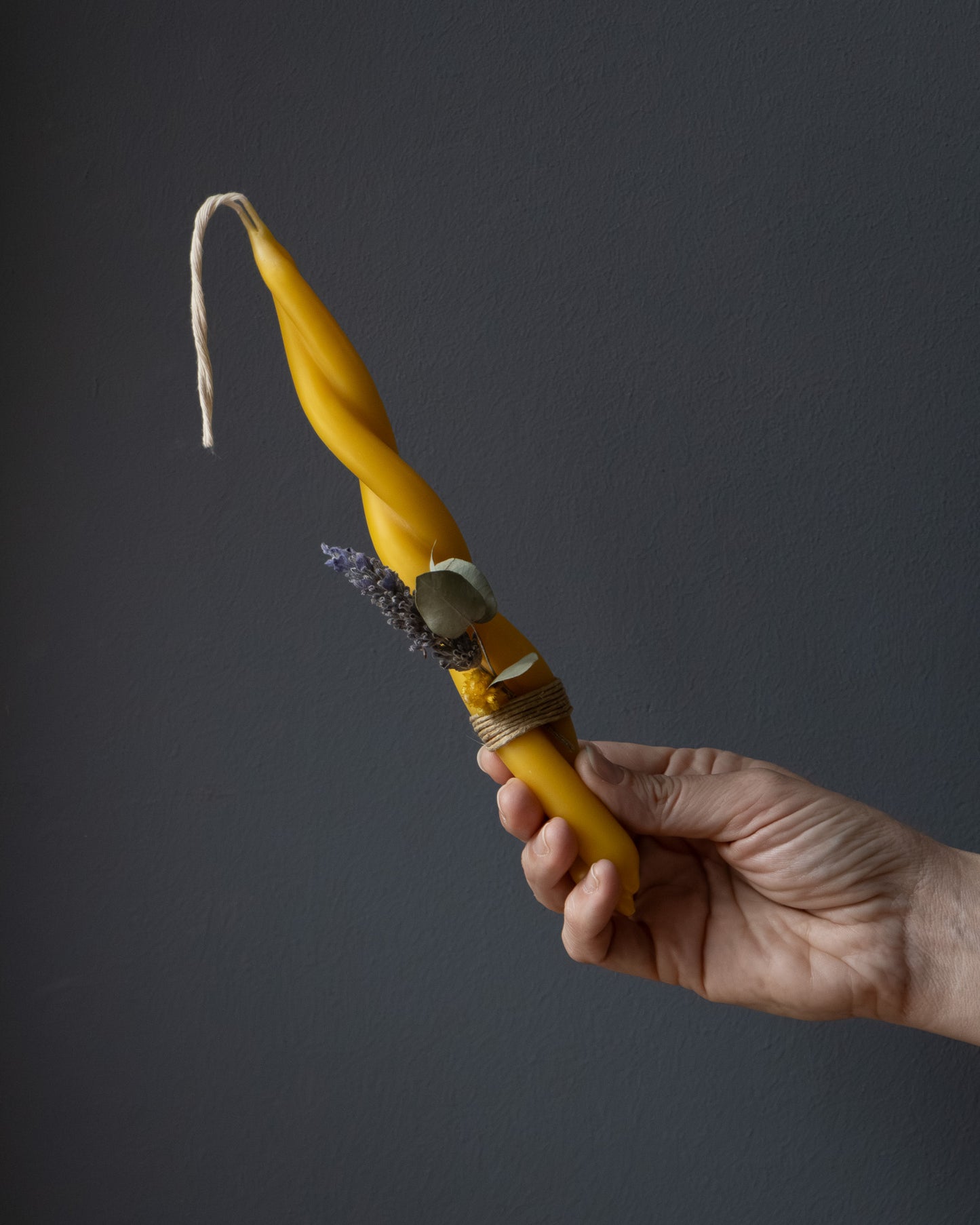 Hand holding a small twisted beeswax candle with eucalyptus and lavender