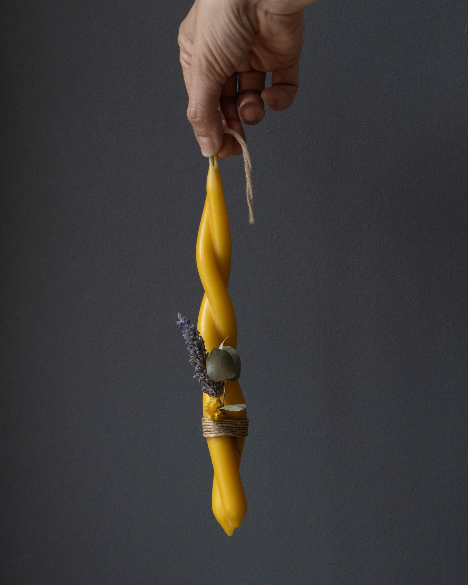 Hand holding a small twisted beeswax candle with eucalyptus and lavender