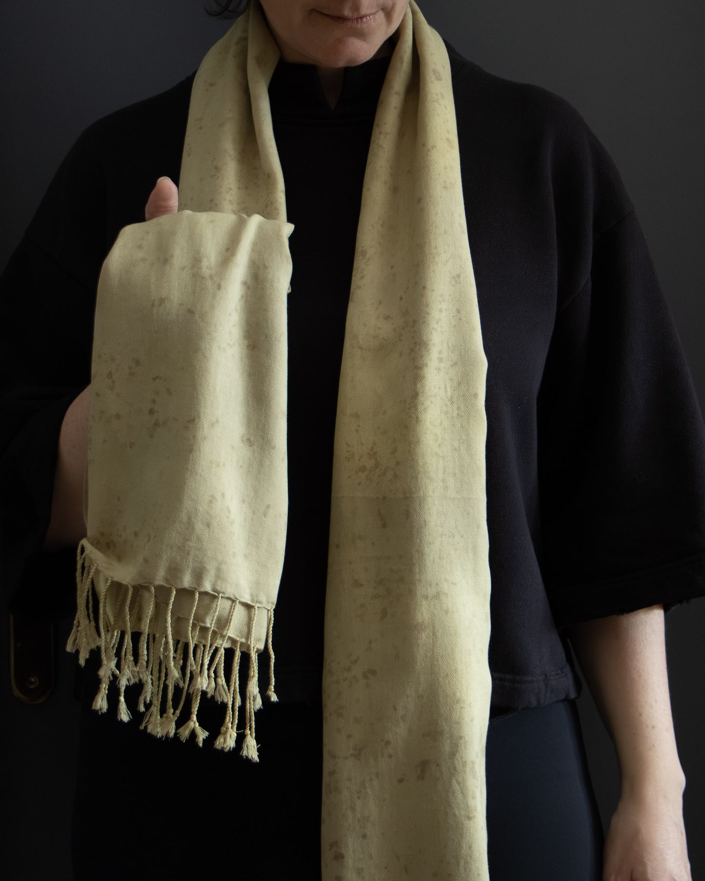 Person holding a naturally dyed cotton scarf with tassels against a dark background