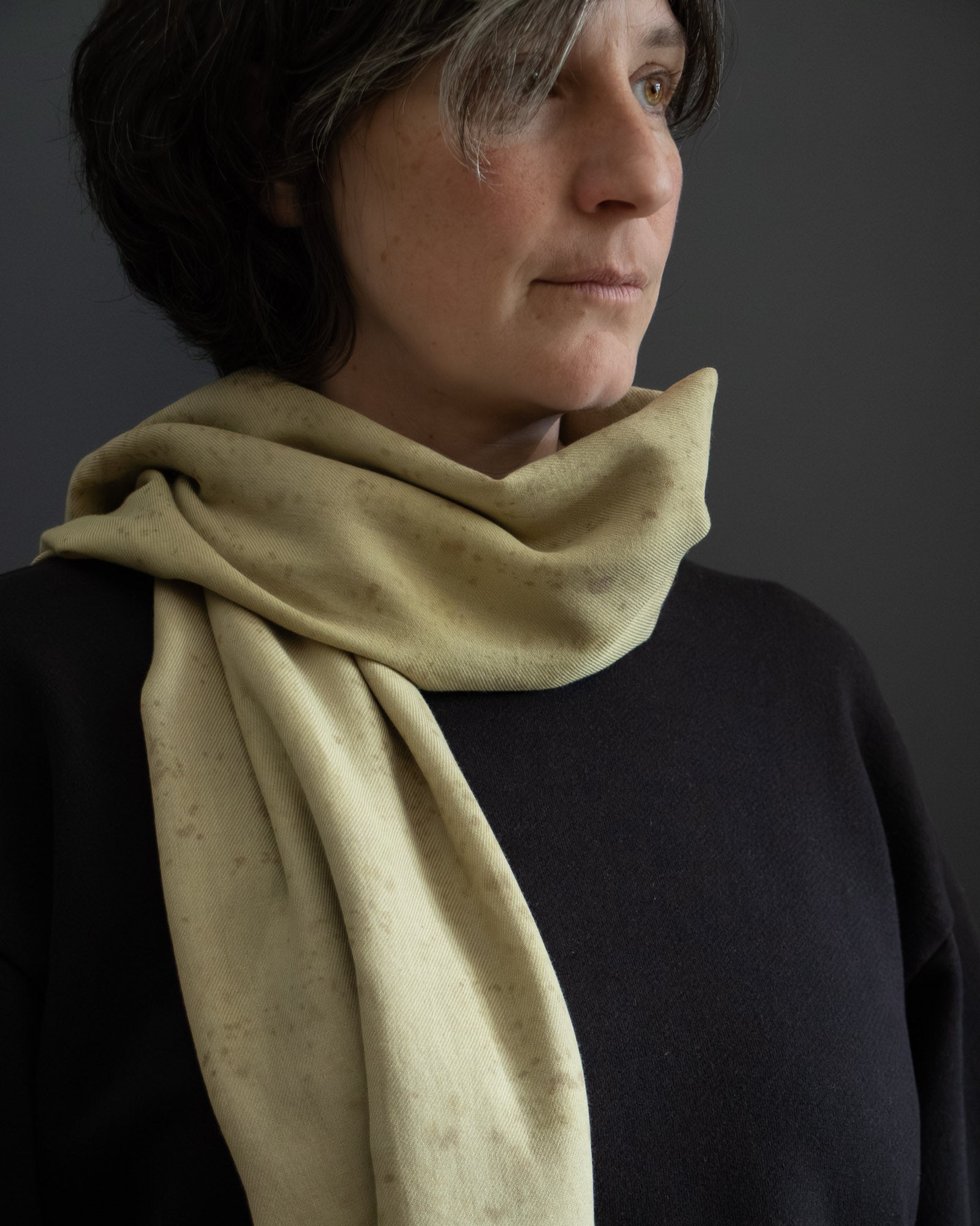 Woman wearing a light green cotton scarf against a dark background