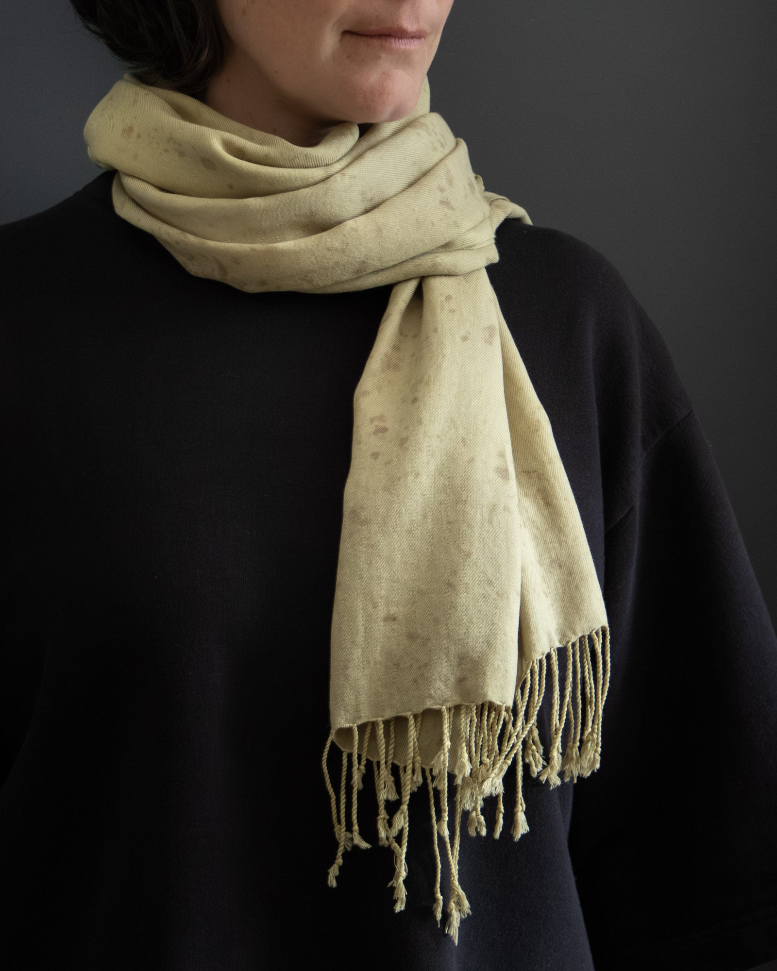 Person wearing a naturally dyed scarf with fringes on a dark background