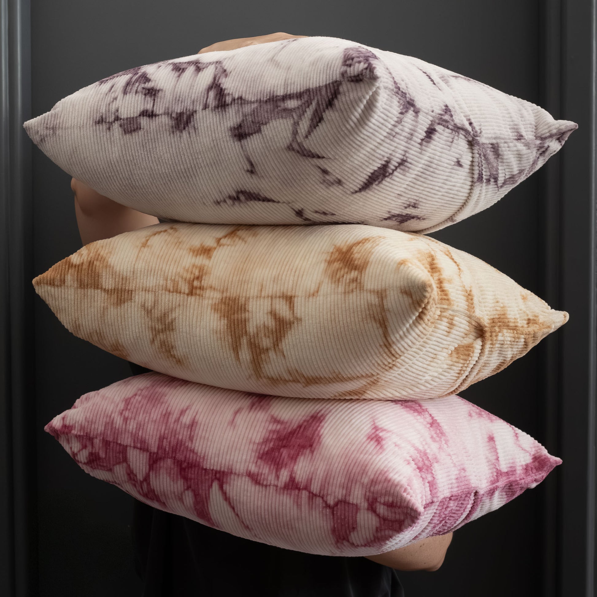Stack of naturally dyed corduroy cushion covers in fuchsia pink, beige and brown, and purple tie-dye patterns.
