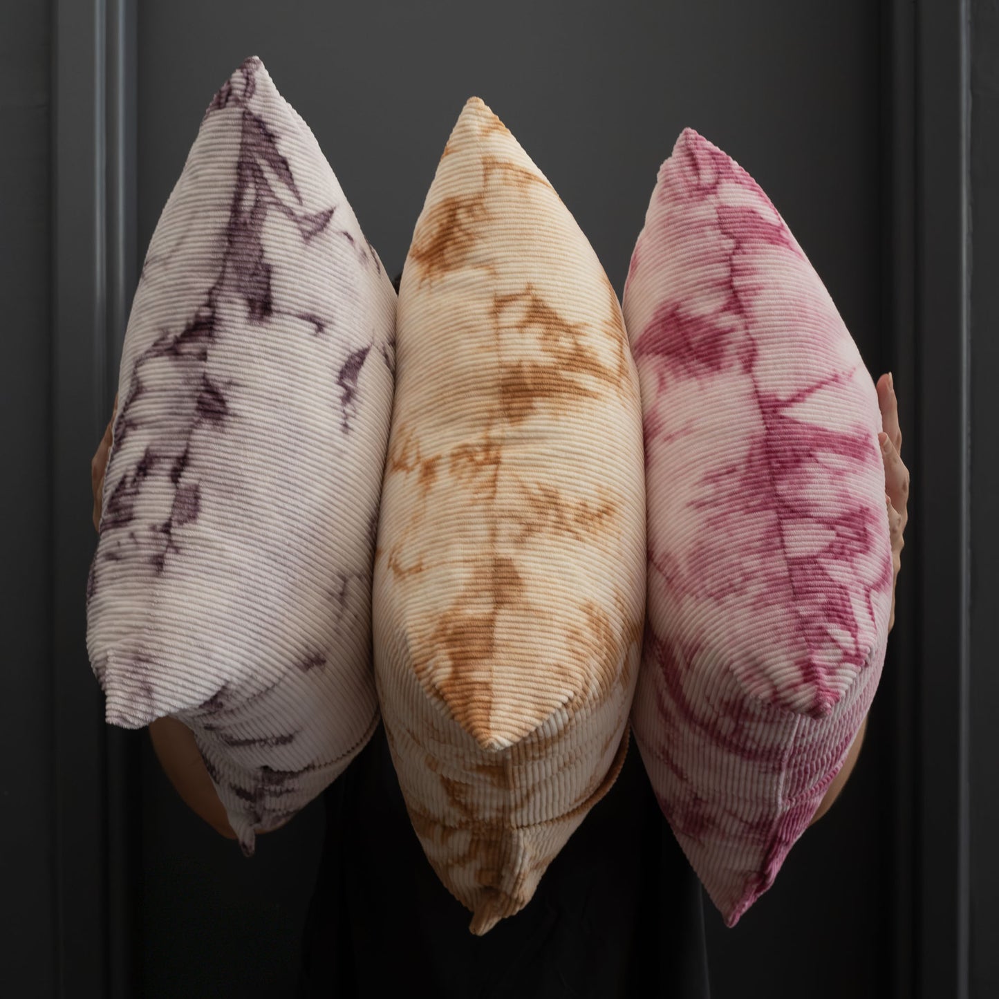 Three decorative pillows with naturally dyed tie-dye patterns on a dark background.