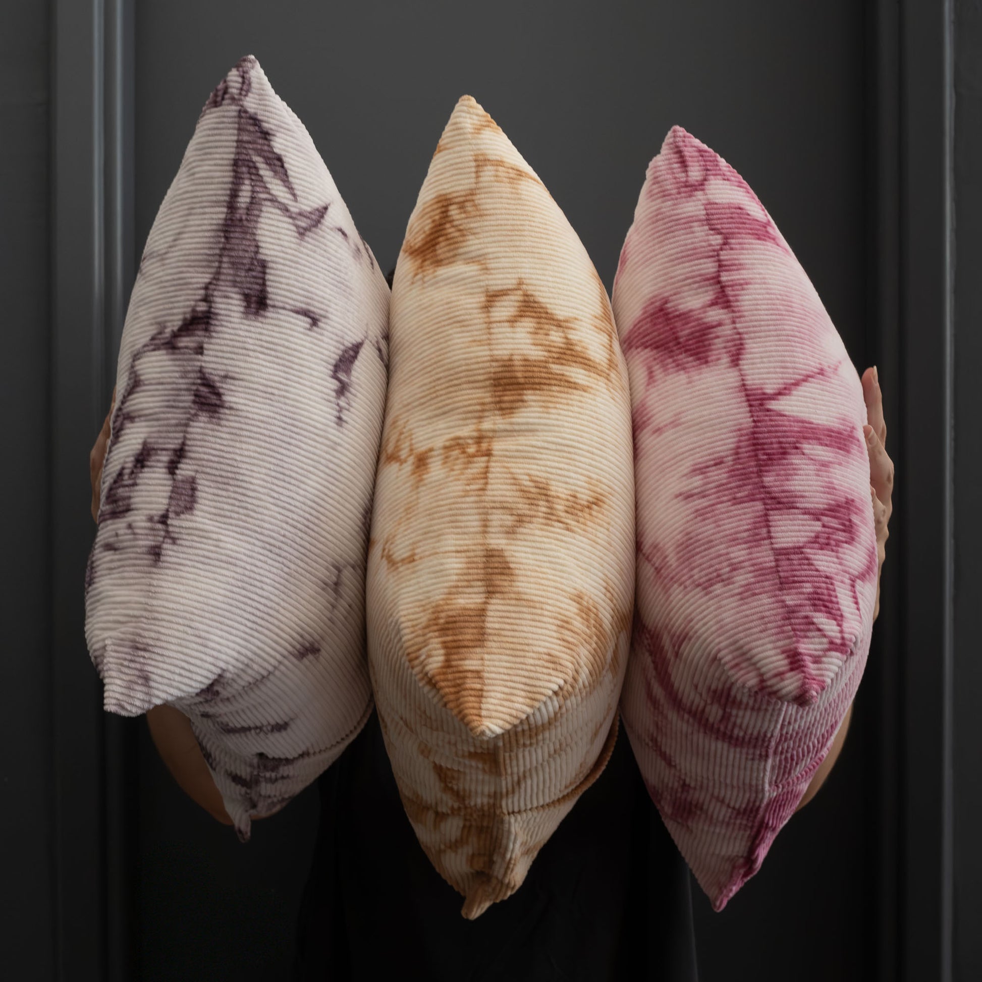 Three decorative pillows with naturally dyed tie-dye patterns on a dark background.