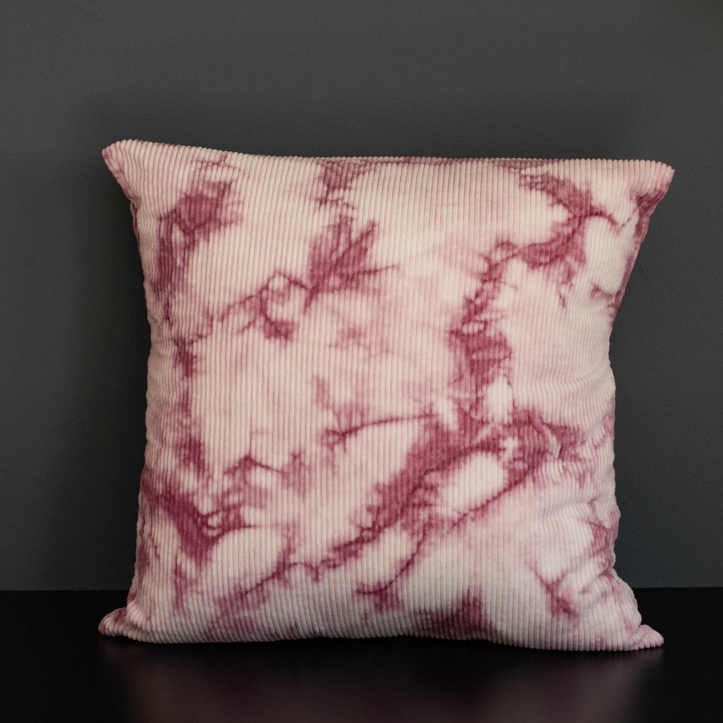 Decorative pillow, naturally dyed corduroy cushion cover in pink cochineal tie-dye pattern on a dark background.