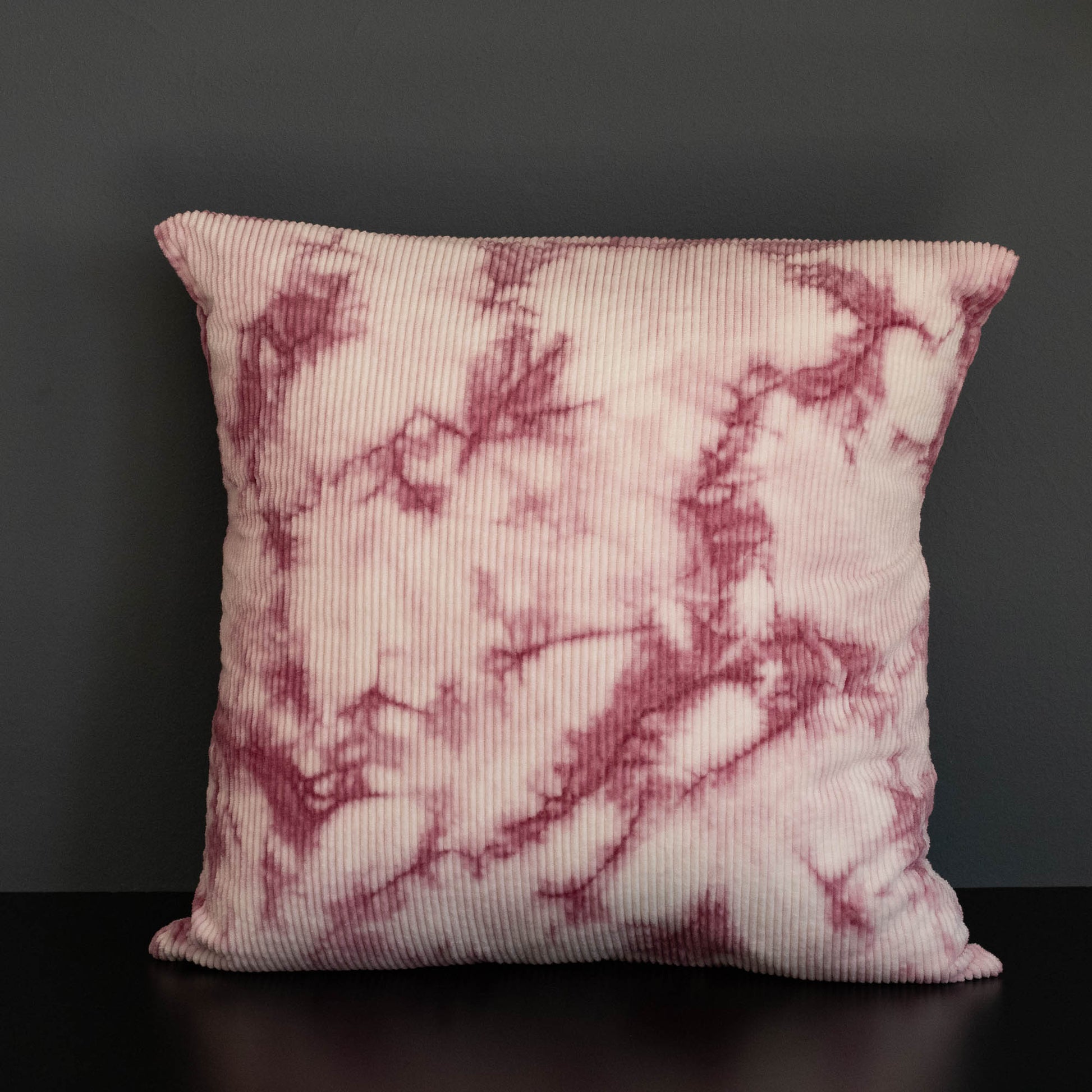 Decorative pillow, naturally dyed corduroy cushion cover in pink cochineal tie-dye pattern on a dark background.