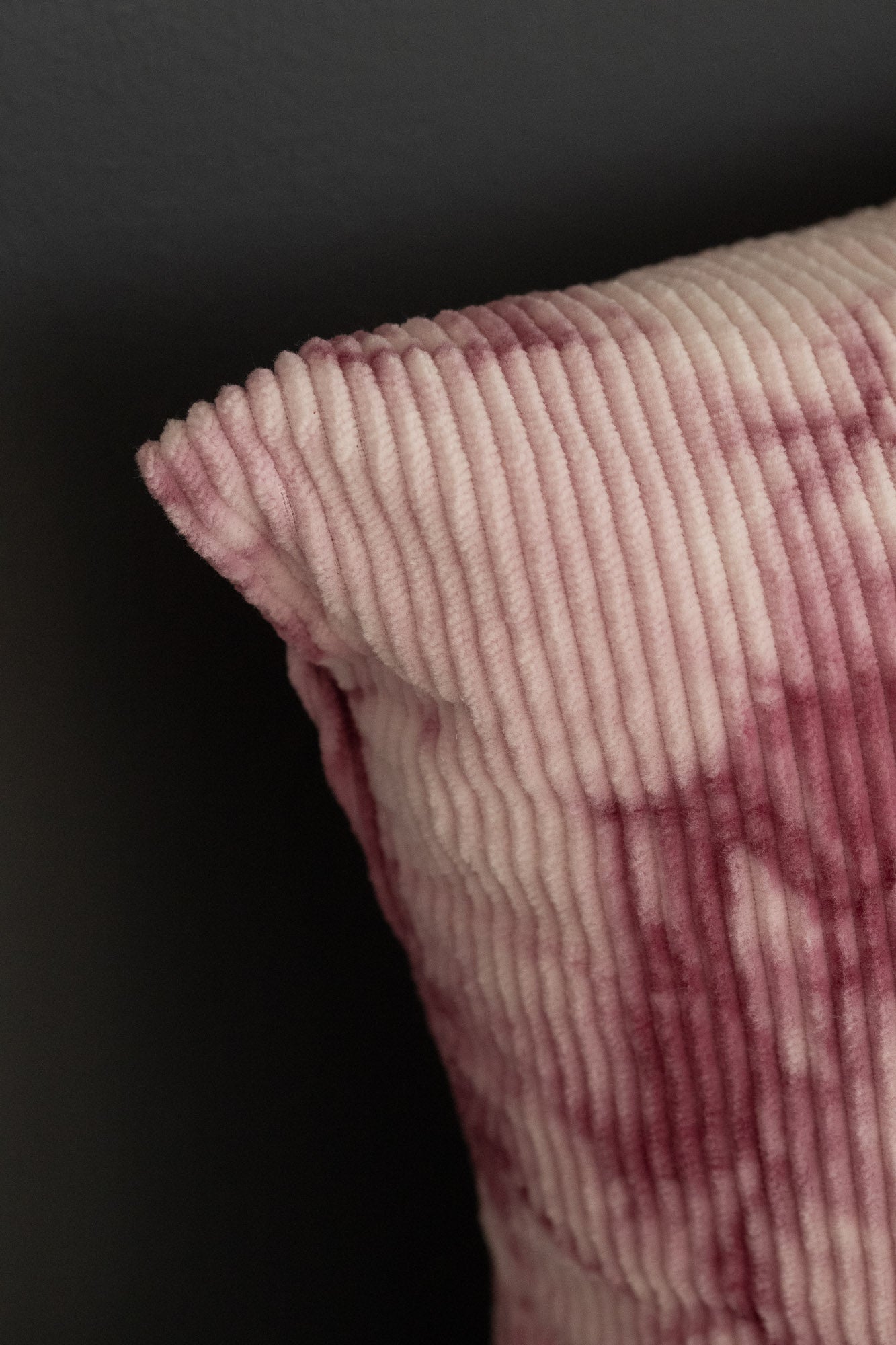 Close-up of a naturally dyed corduroy cushion cover with fuchsia pink cochineal tie-dye patterns.