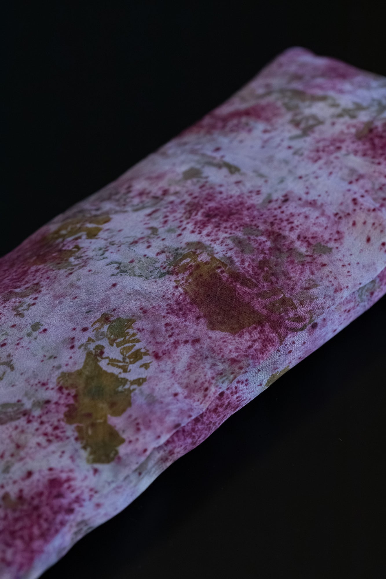 Close-up of naturally dyed silk eye pillow in deep fuchsia and mauve tones from cochineal and logwood, with onion-skin and rose petal imprints on Greek mulberry silk.
