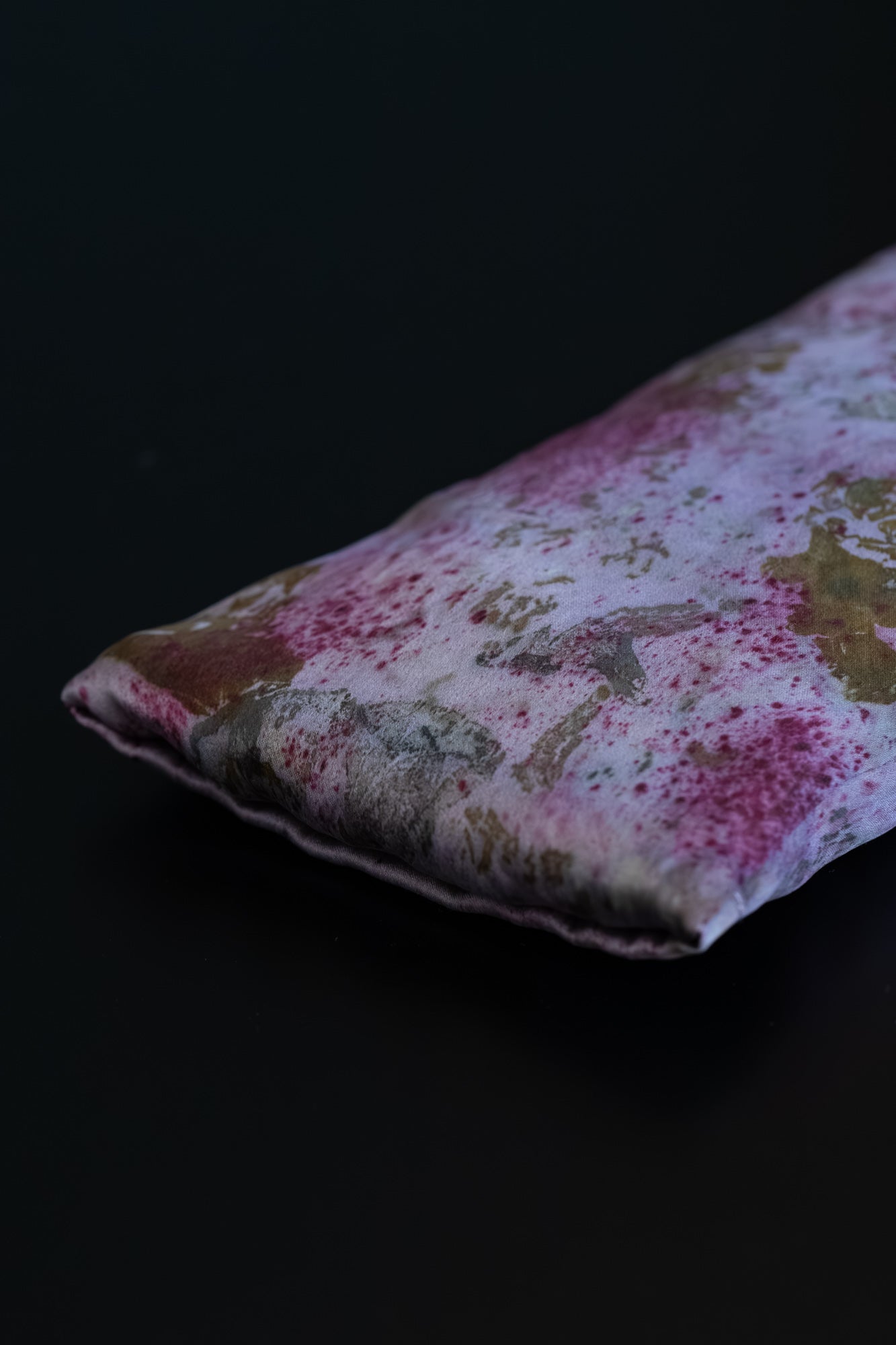 Close-up of naturally dyed silk eye pillow in deep fuchsia and mauve tones from cochineal and logwood, with onion-skin and rose petal imprints on Greek mulberry silk.