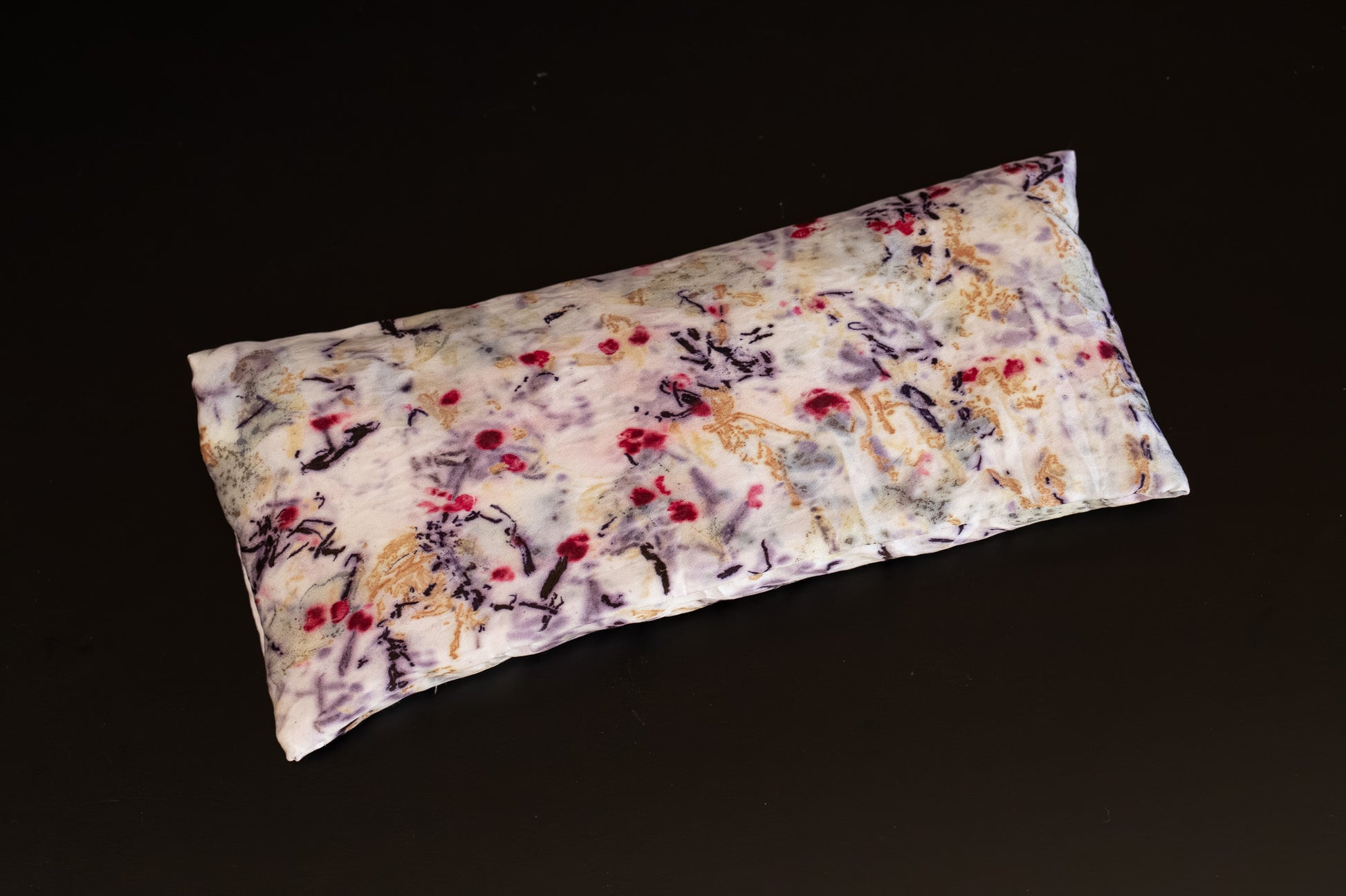 Naturally dyed silk eye pillow photographed flat, featuring bold multi-coloured imprints.
