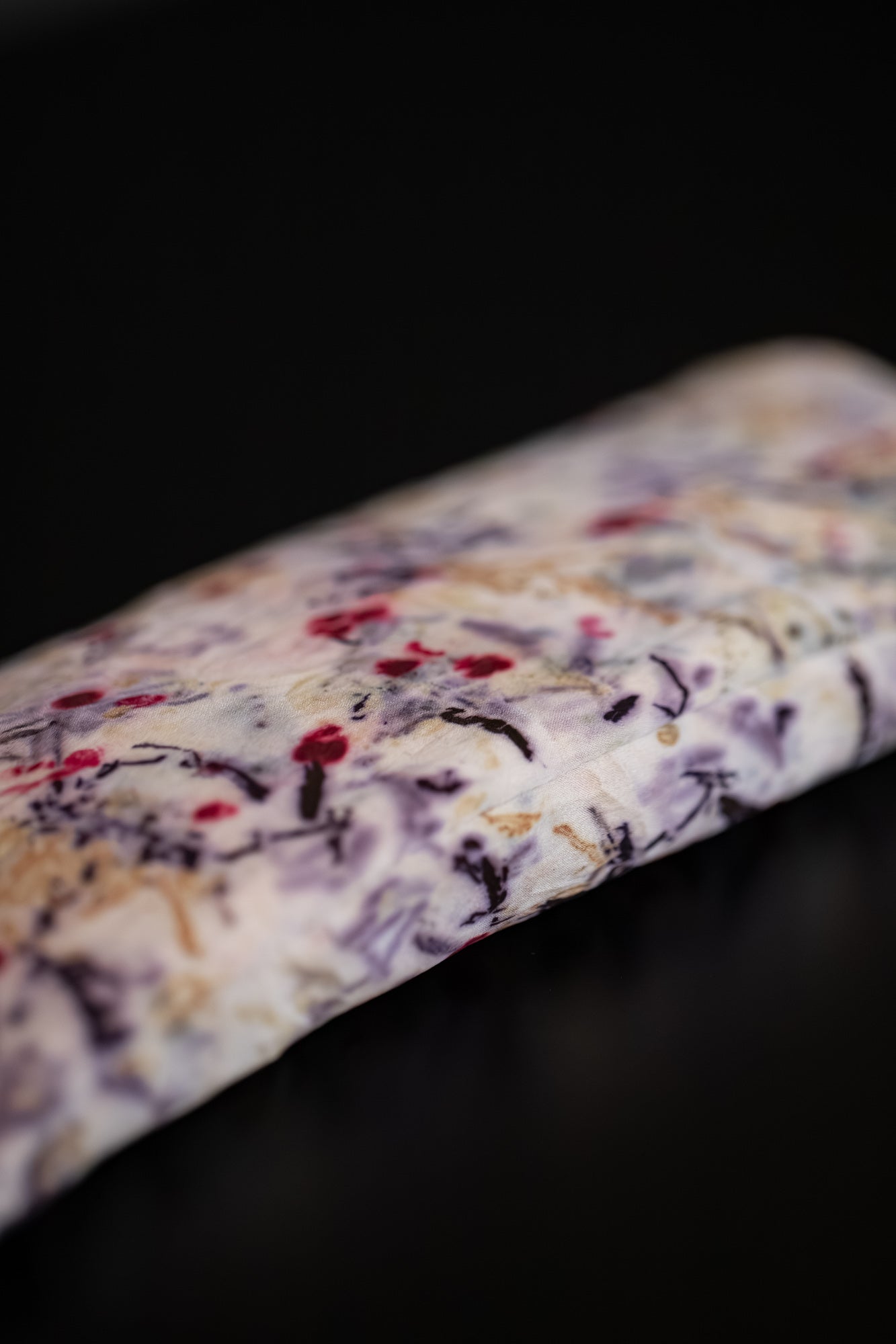 Close-up of a naturally dyed silk eye pillow with vivid purple, red and golden botanical imprints.