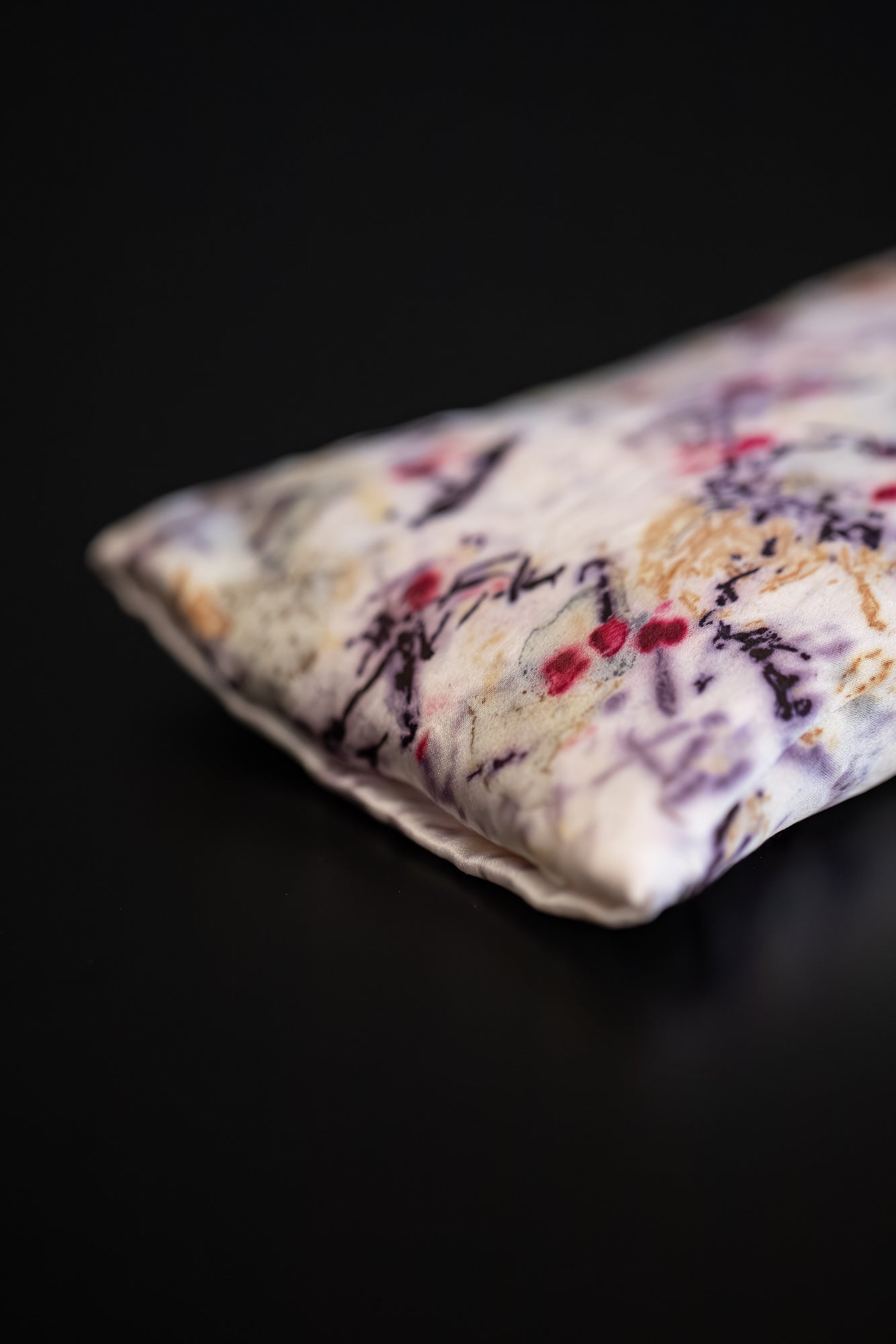 Detailed view of a one-of-a-kind silk eye pillow showing strong natural dye marks in red, purple and gold.